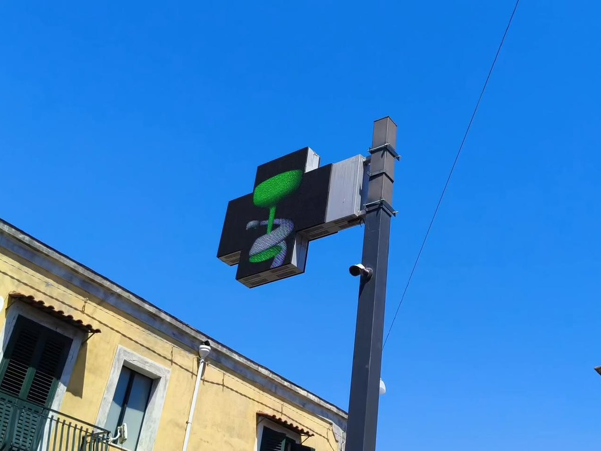 Outdoor LED pharmacy cross sign on a street pole in daylight