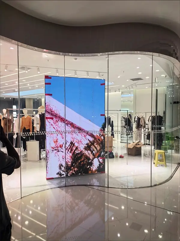 Floor-standing LED display in curved glass storefront, clothing store.webp