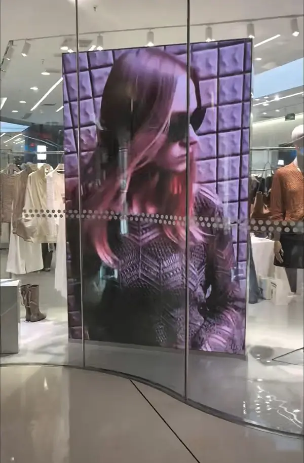 Floor-standing LED display showing fashion content in curved glass facade.webp